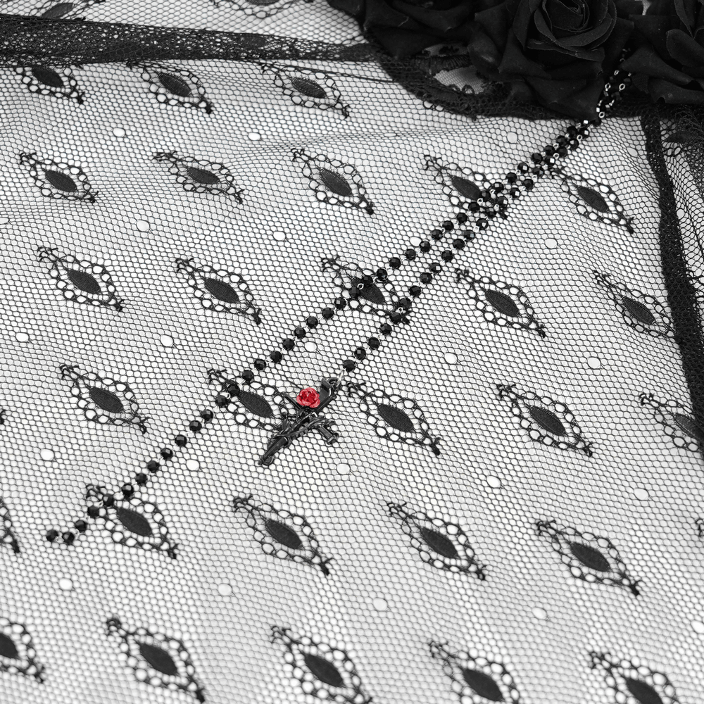 Close-up of gothic lace veil featuring floral accents and a cross pendant with red detail on sheer black fabric.
