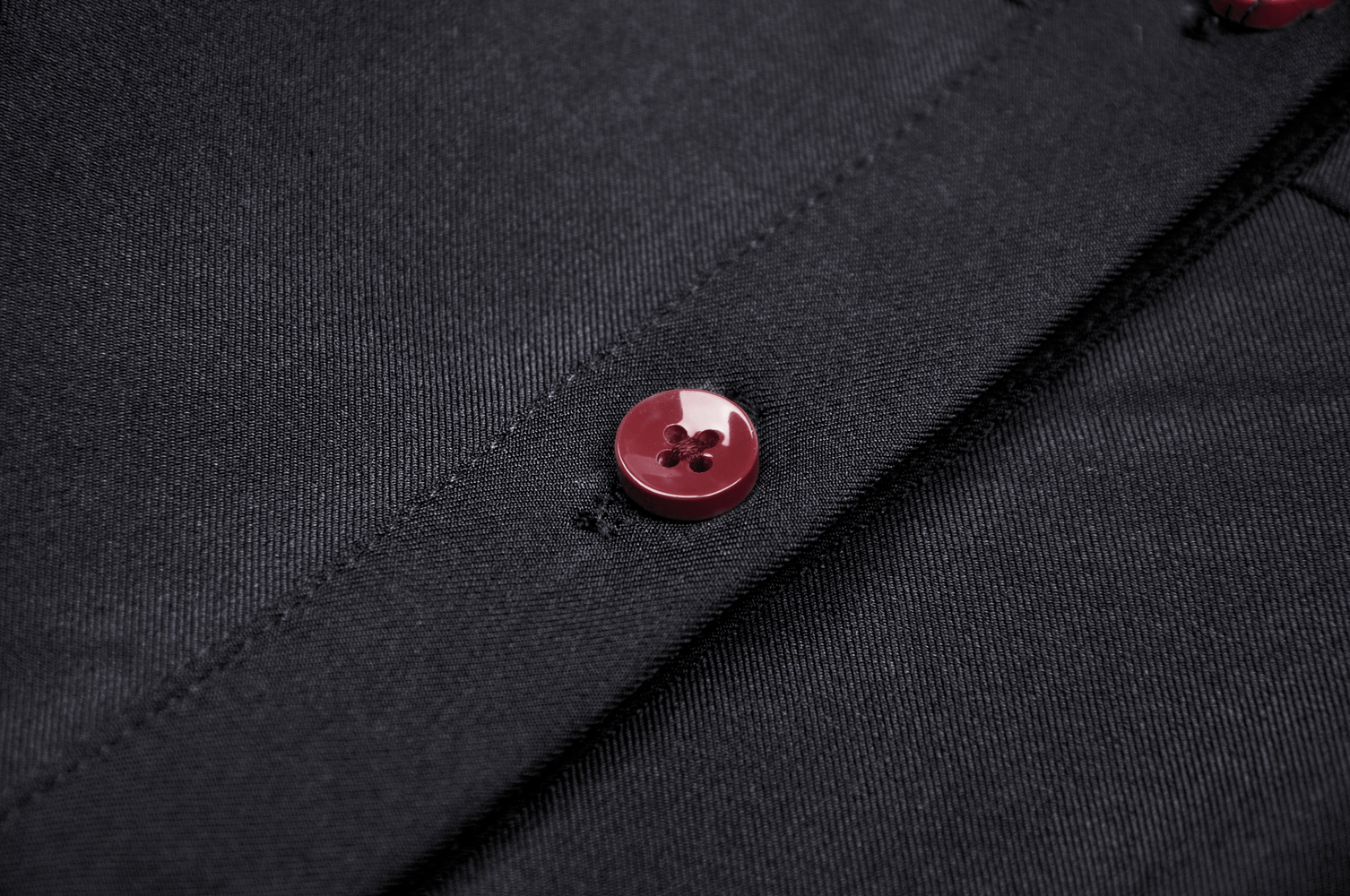 Close-up of a red button on a gothic black dress fabric, showcasing elegant detailing and craftsmanship.