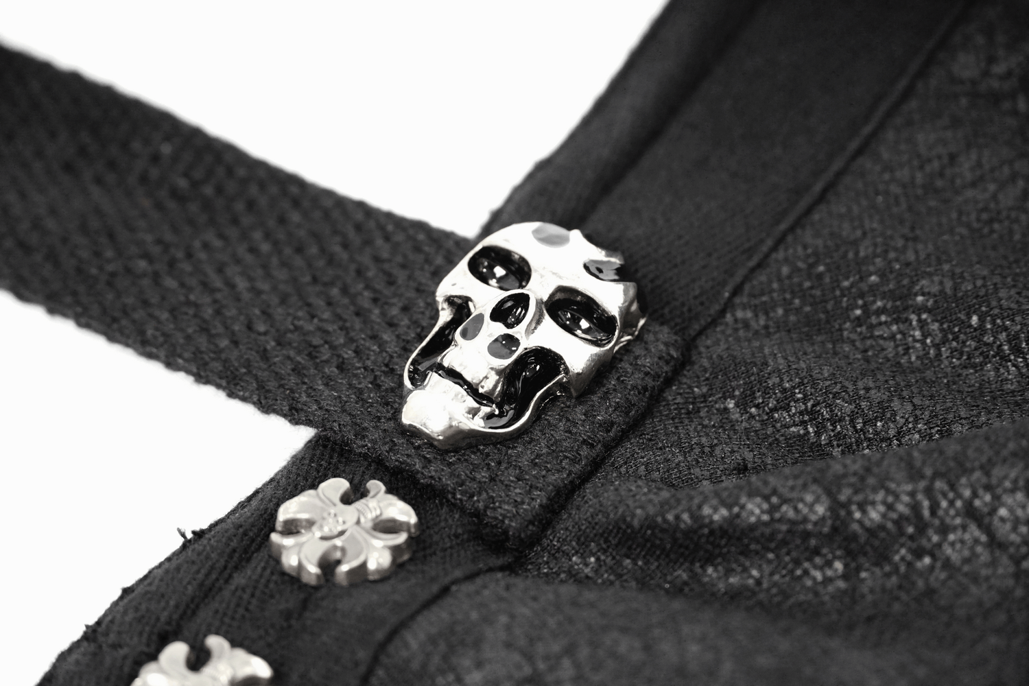 Close-up of a gothic cloak detailing featuring a silver skull button and ornate clasps, ideal for edgy fashion.