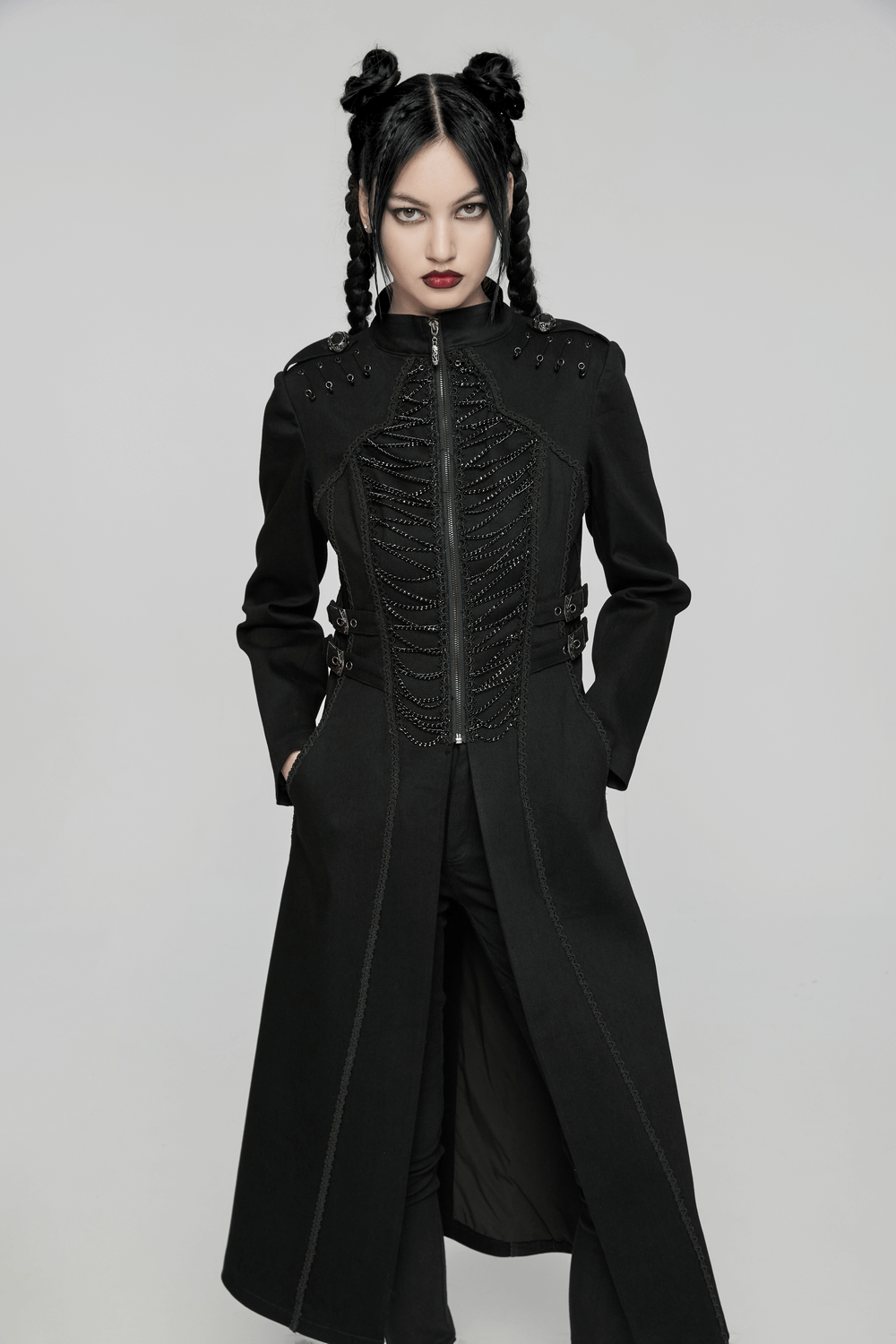 Gothic long coat with chains and intricate buckles, worn by a model with dark braids and bold makeup.