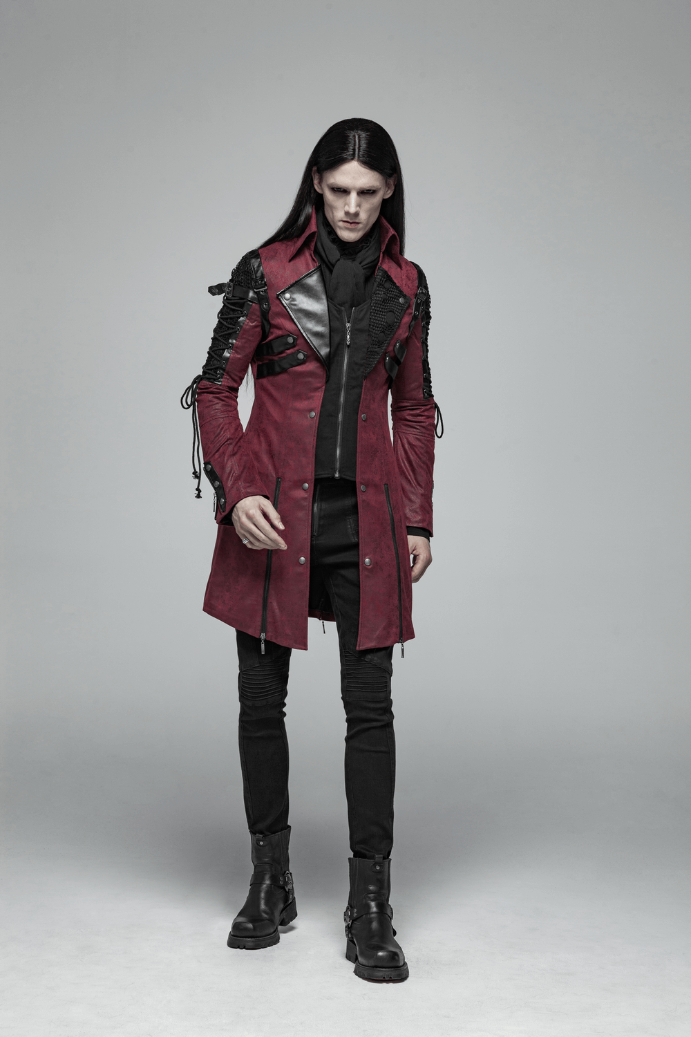 Gothic male model wearing a burgundy leather trench coat with laced sleeves and stylish black attire.