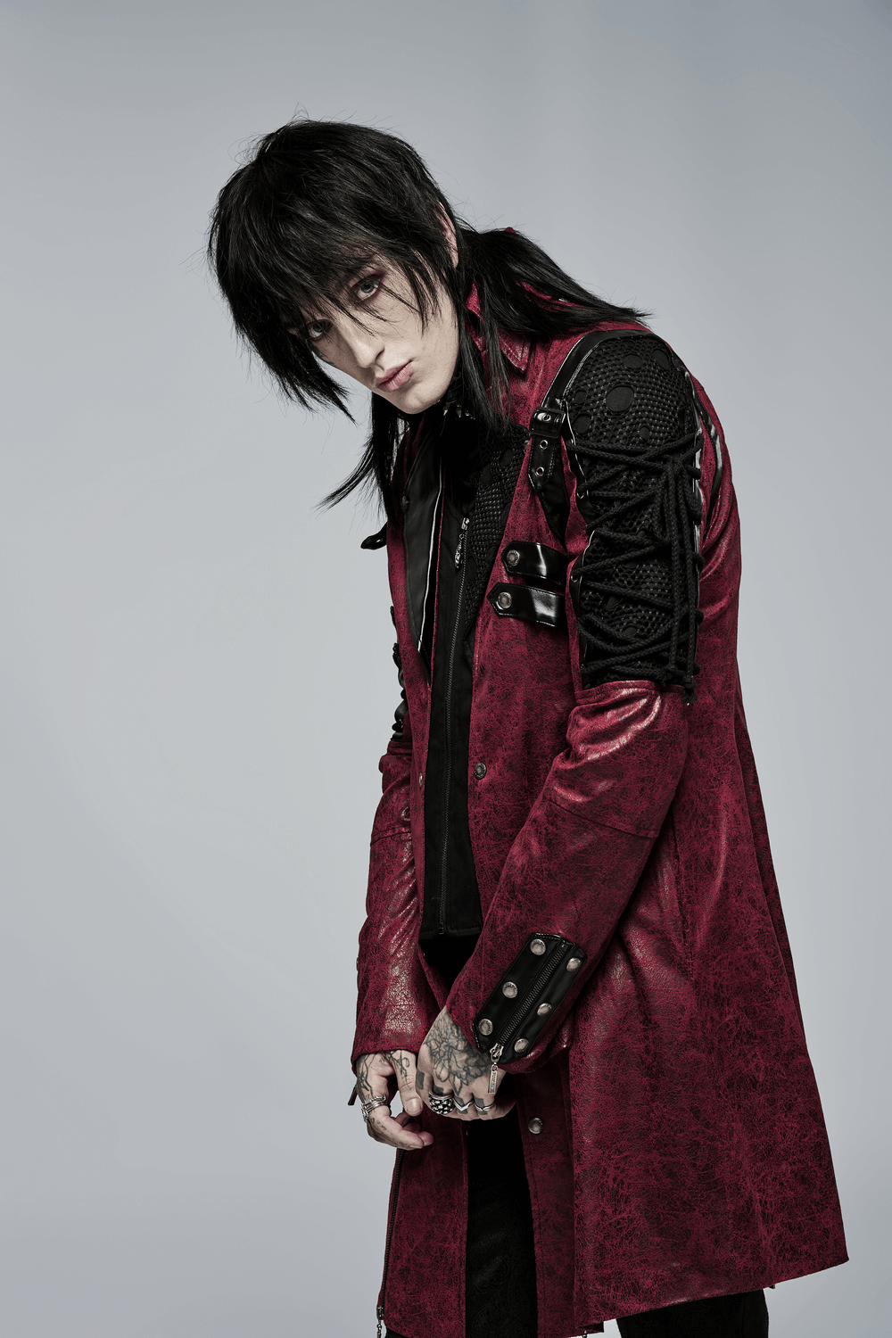 Gothic male in striking burgundy leather trench coat with laced sleeves, exuding dark elegance and style.