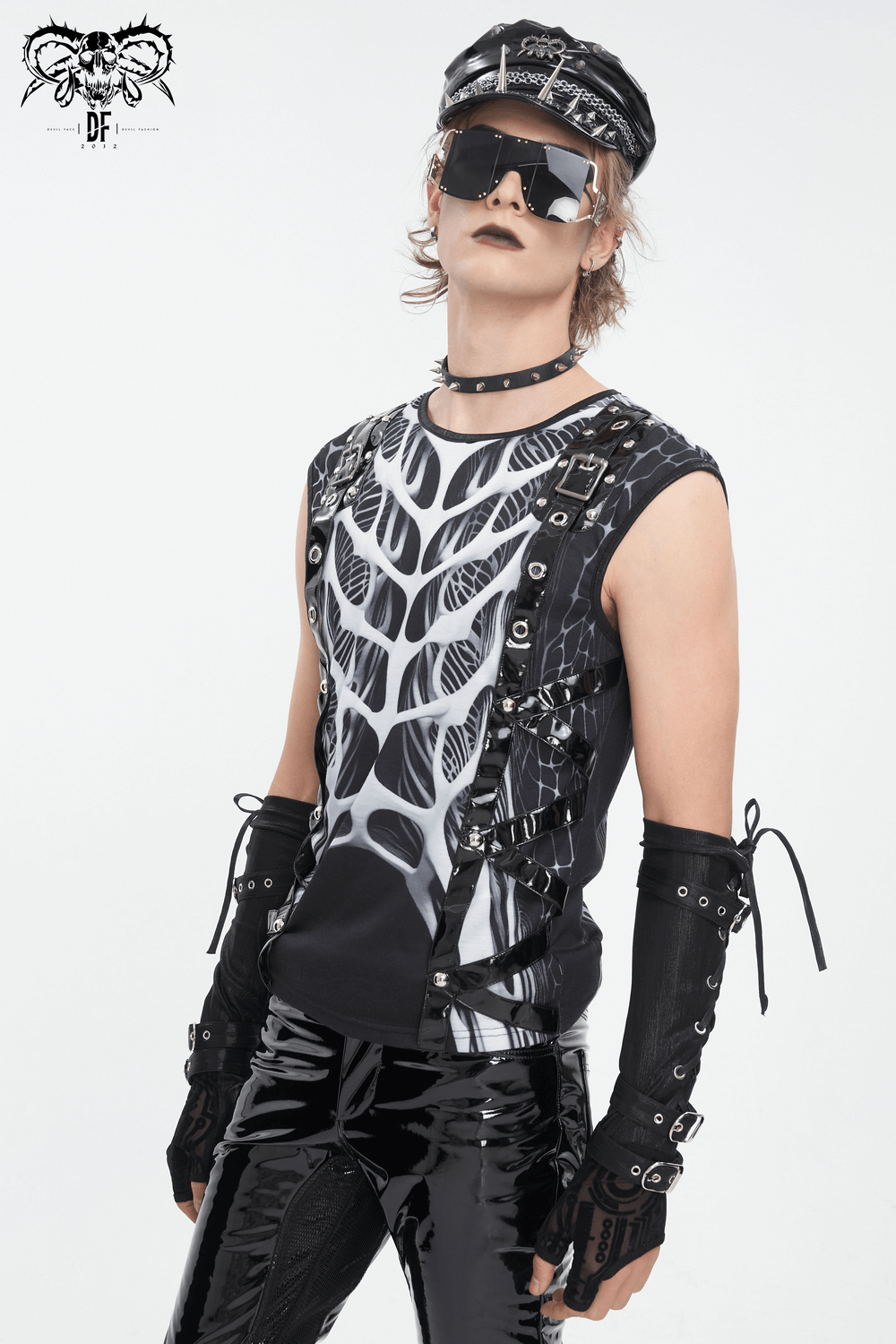 Gothic male model wearing a skeleton print tank top, black shiny pants, and stylish accessories for an edgy look.
