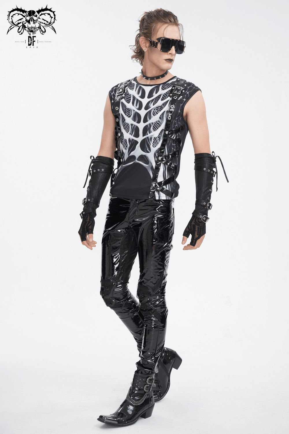 Gothic male model in black tank top with skeleton print and shiny pants, exuding edgy rockstar vibes.