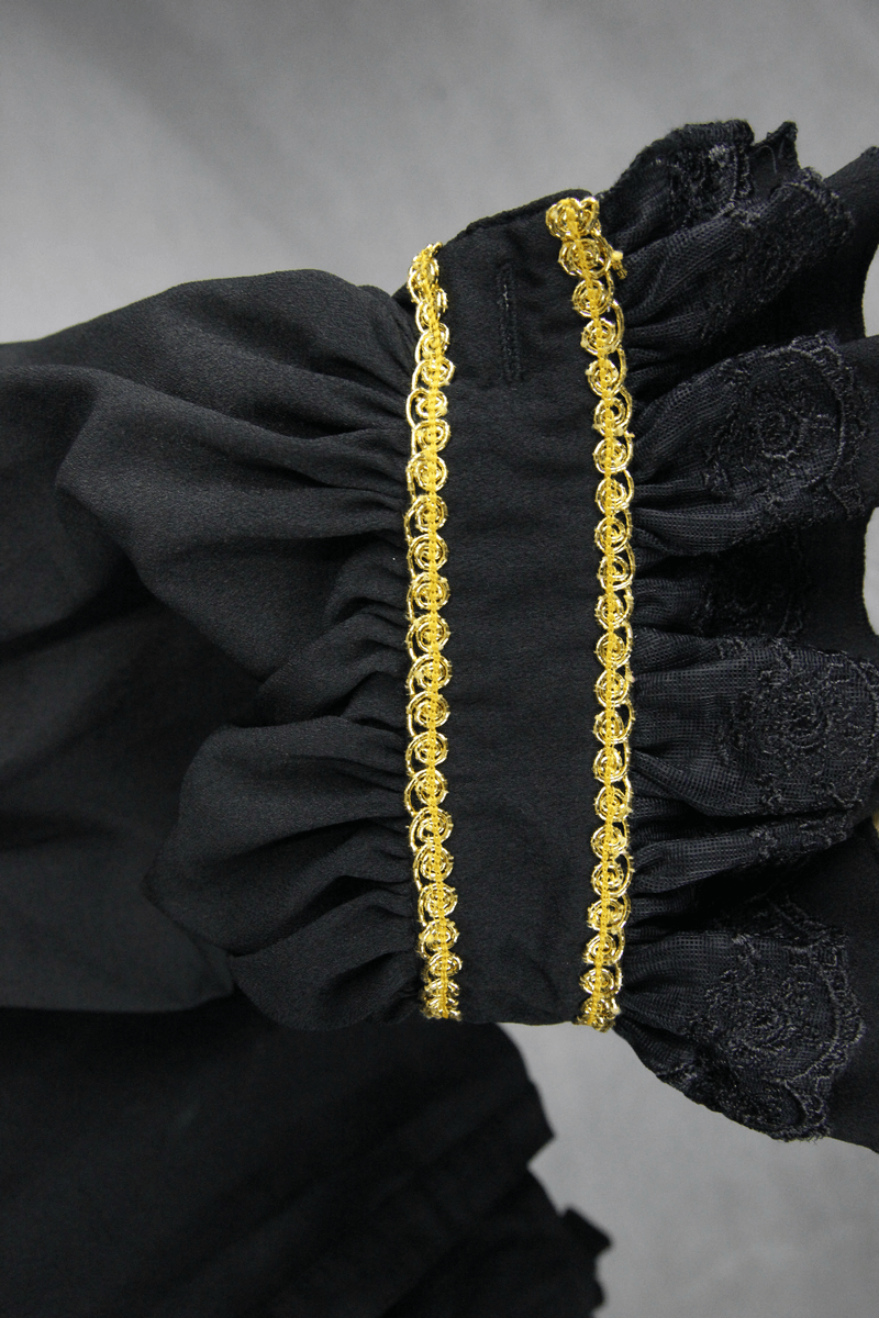 Close-up of gothic men's shirt sleeve, black fabric with gold trim and intricate detailing.