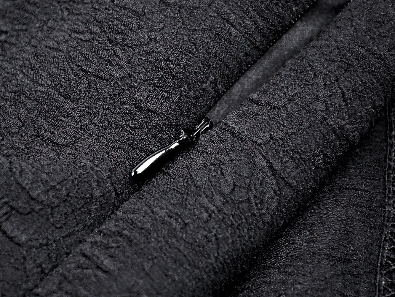 Close-up of black lace fabric with a zipper detail, showcasing intricate texture and elegance for gothic fashion.