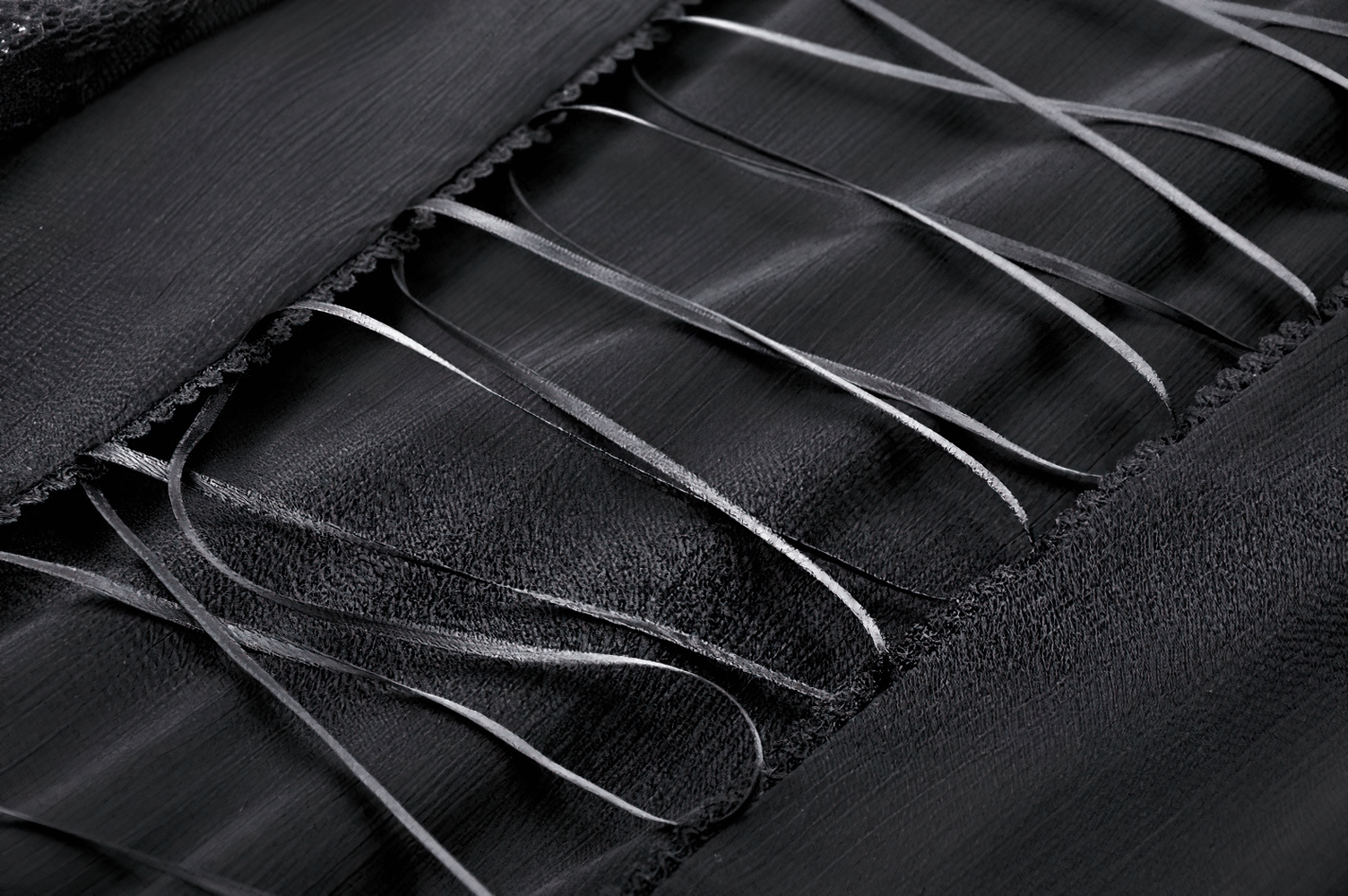 Close-up of black chiffon fabric with elegant lace detailing and flowing ribbons for gothic fashion.
