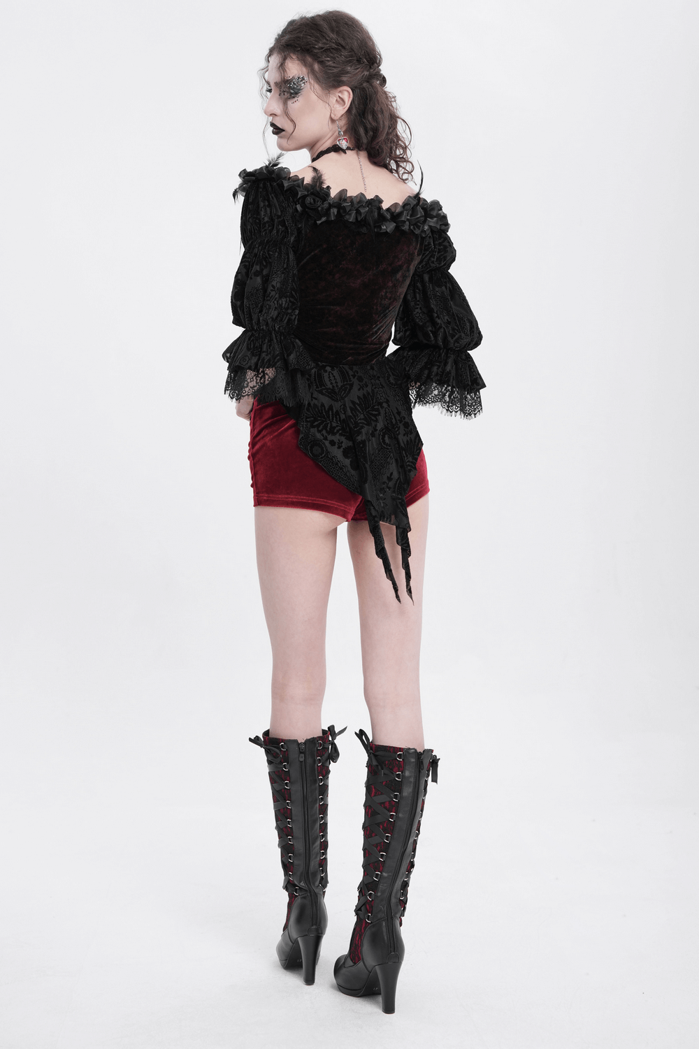 Gothic off-shoulder lace-up velvet blouse with ruffled sleeves and floral details, paired with short red shorts and knee-high boots.