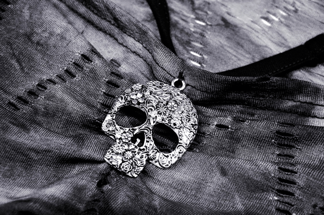 Close-up of a stylish silver skull pendant on a dark fabric, showcasing edgy punk fashion details.