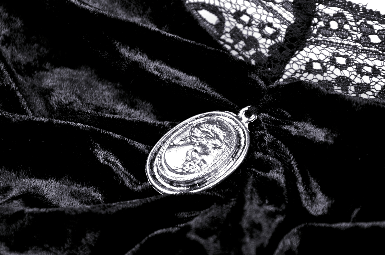 Close-up of a vintage cameo detail on a gothic off-shoulder velvet top with black lace sleeves.
