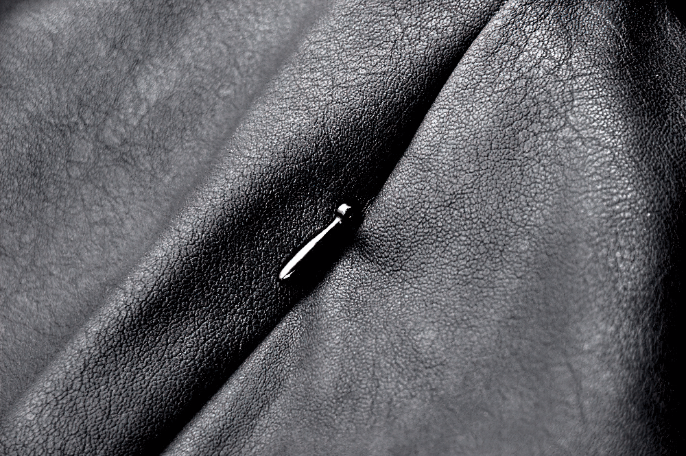 Close-up of textured black faux leather with a silver buckle accent for a punk-style mini skirt.