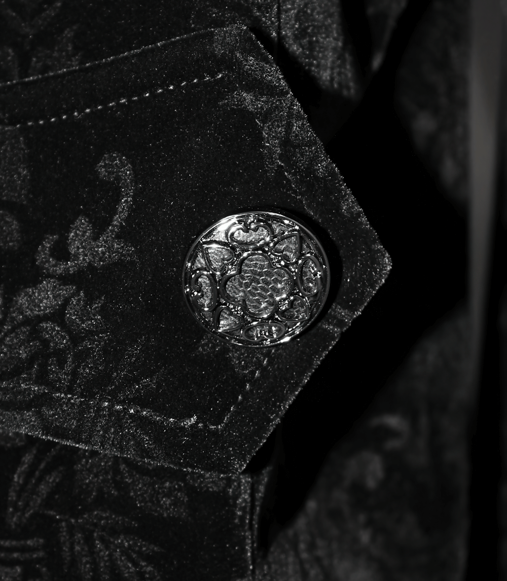 Close-up of an ornate silver button on women's black gothic retro puff sleeve jacket with intricate lace detail.