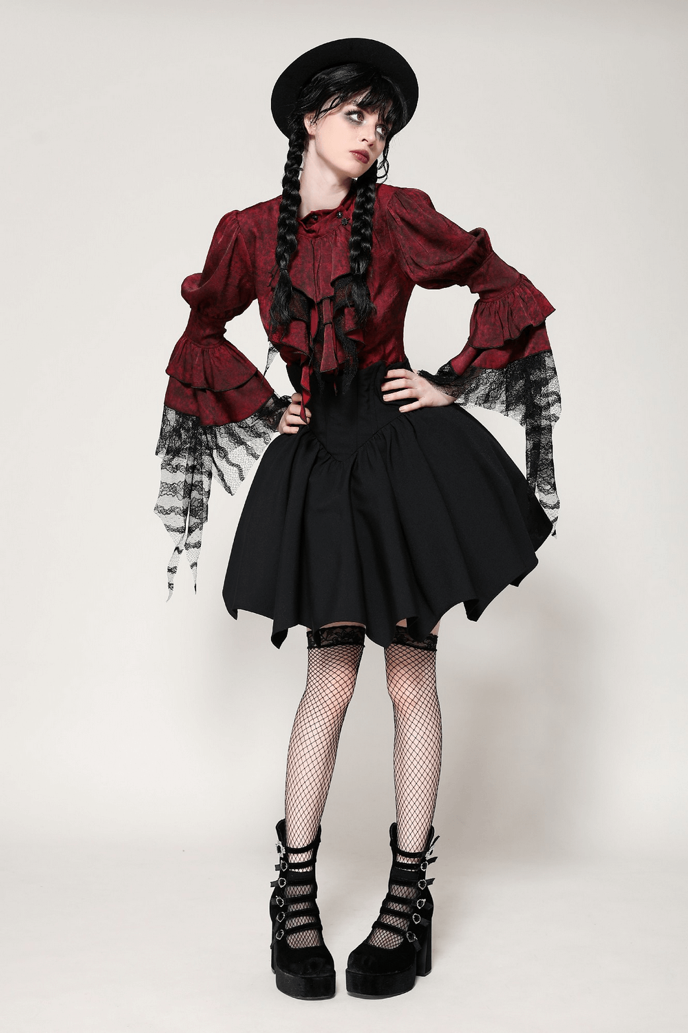 Woman in gothic fashion wearing a red blouse and black A-line skirt with fishnet stockings and platform boots.