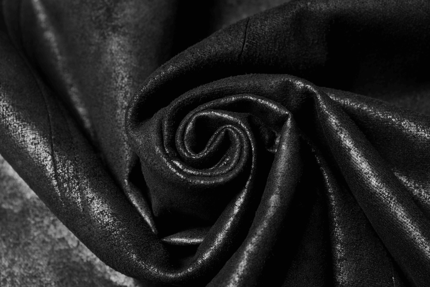 Close-up of black leather fabric showcasing its glossy texture and intricate details, perfect for gothic cape designs.
