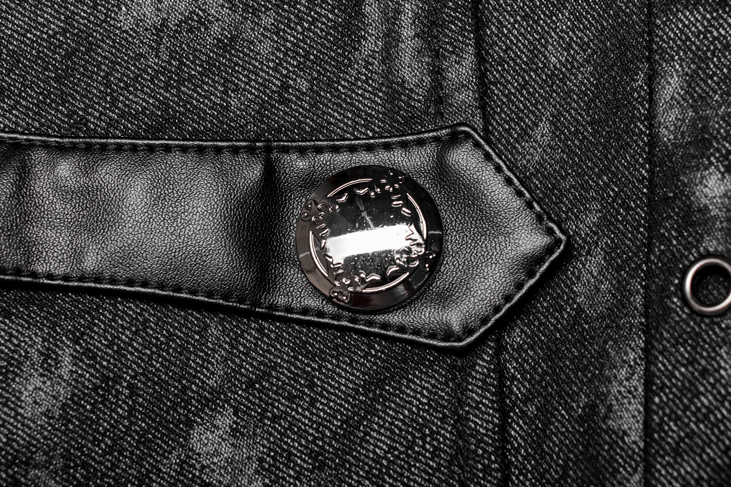 Close-up of a stylish black button and fabric tab detail on a gothic coat, showcasing intricate design elements.