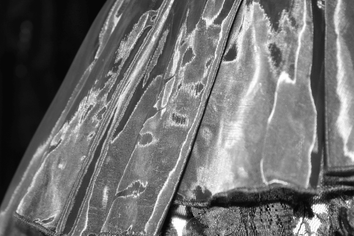 Close-up of a lightweight gothic style top with shimmering lace and asymmetric design in black.