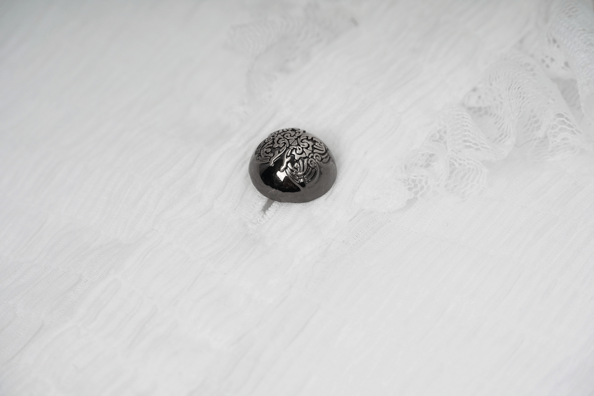 Close-up of a decorative button on a white gothic style shirt with lace detailing.