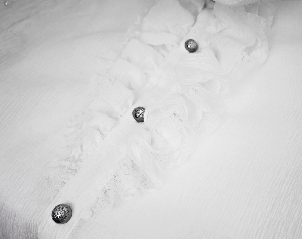 Close-up of gothic white shirt with ruffles and stylish buttons, highlighting vintage lace details for men.
