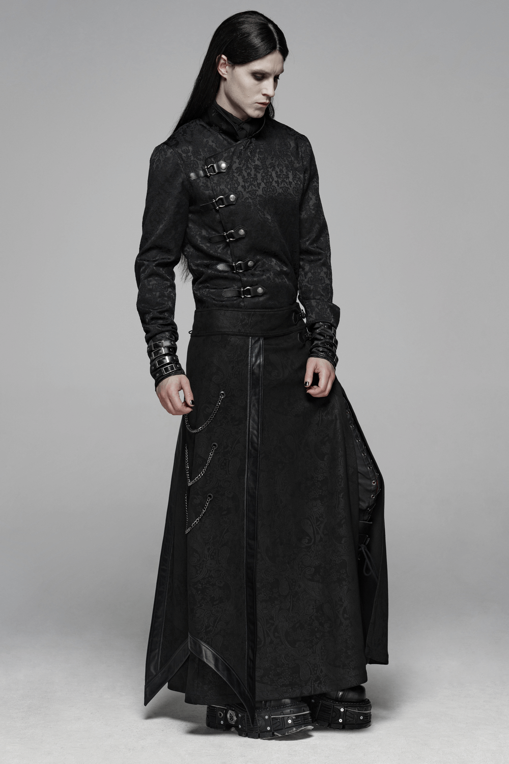 Man in gothic floral long overskirt with buckles and chains, showcasing dark elegance and alternative fashion.