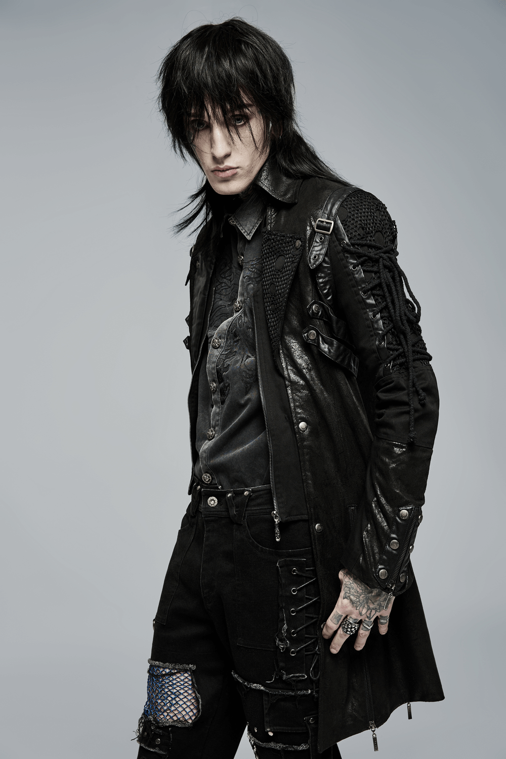 Stylish man in a black gothic trench coat with lacing, showcasing a punk rock look and edgy accessories.