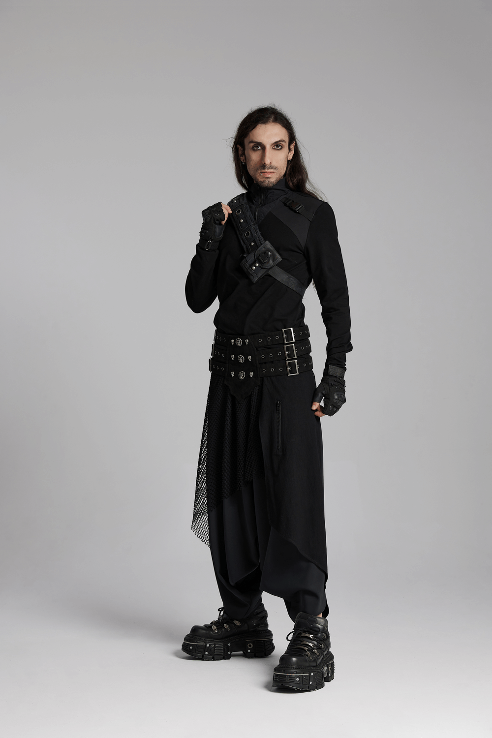 Man in all-black gothic outfit with multiple belts, gloves, and chunky footwear, showcasing a punk-inspired style.