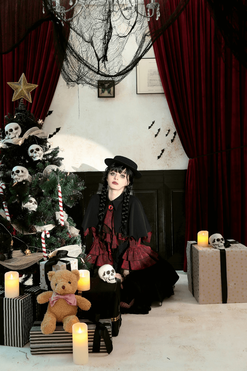 Gothic room with skull decorations, Christmas tree, and candles. Person in dark hat and red dress adds mysterious holiday flair.