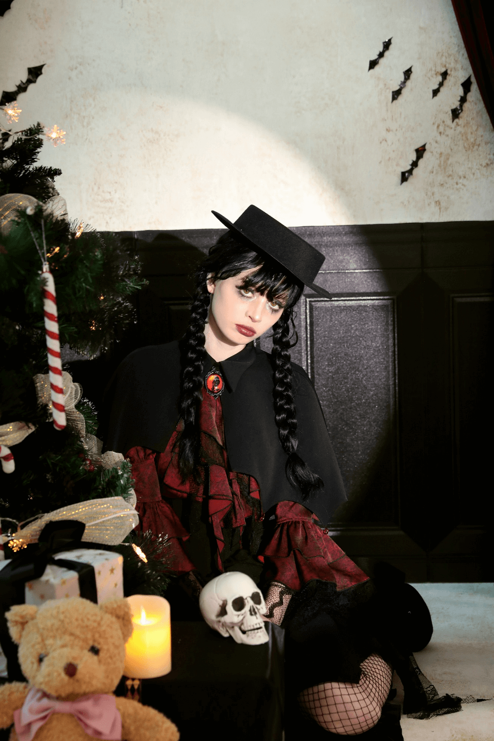 Gothic vampire cape with high collar and gem clasp worn by a person next to a decorated tree and skull in a dimly lit room.