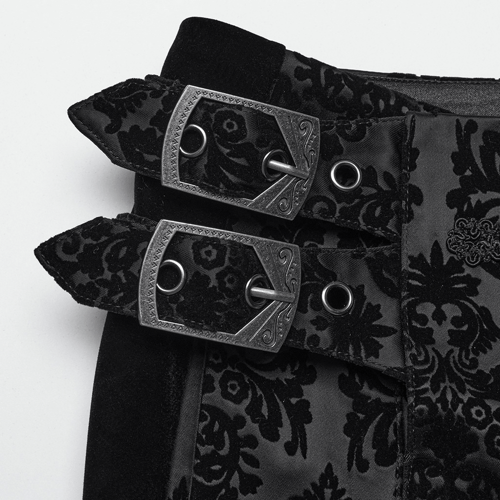 Close-up of ornate gemstone buckles on gothic velvet pants, featuring detailed floral flocking design.