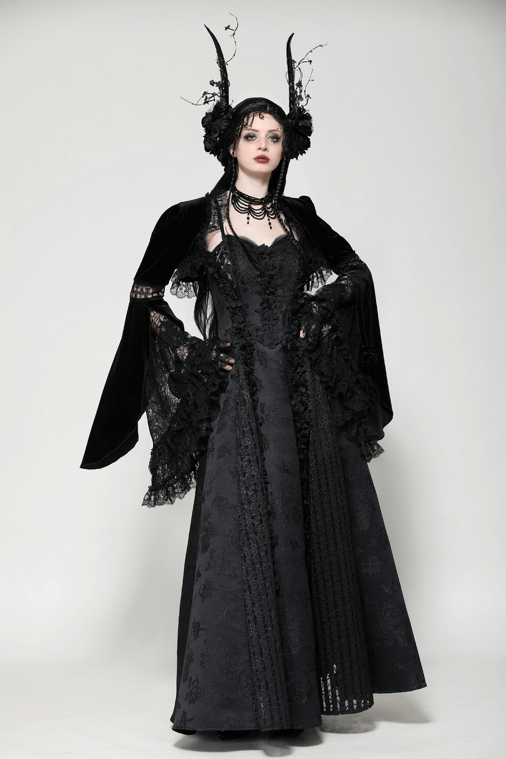 Elegant goth model in black velvet lace bolero and dark gown with flared sleeves and floral accents.
