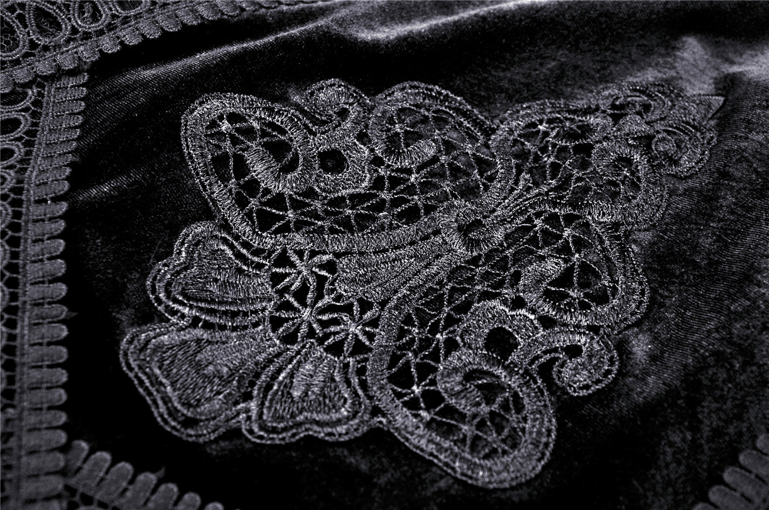 Close-up of intricate black lace embroidery on velvet fabric, capturing Victorian gothic elegance.