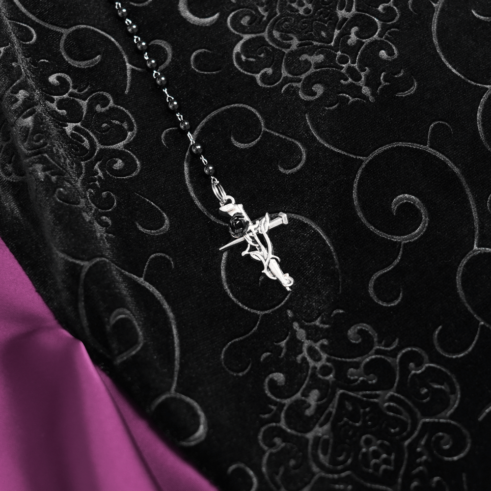 Close-up of silver cross pendant on gothic velvet skirt, featuring intricate black lace and purple satin details.