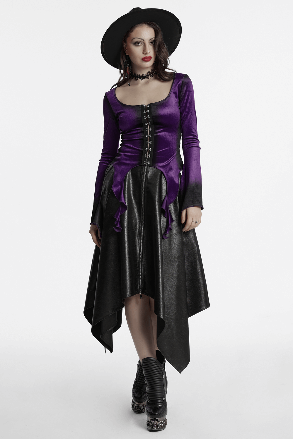 Gothic velvet top with metal buckles and dramatic hem, styled with black skirt and hat for an edgy look.