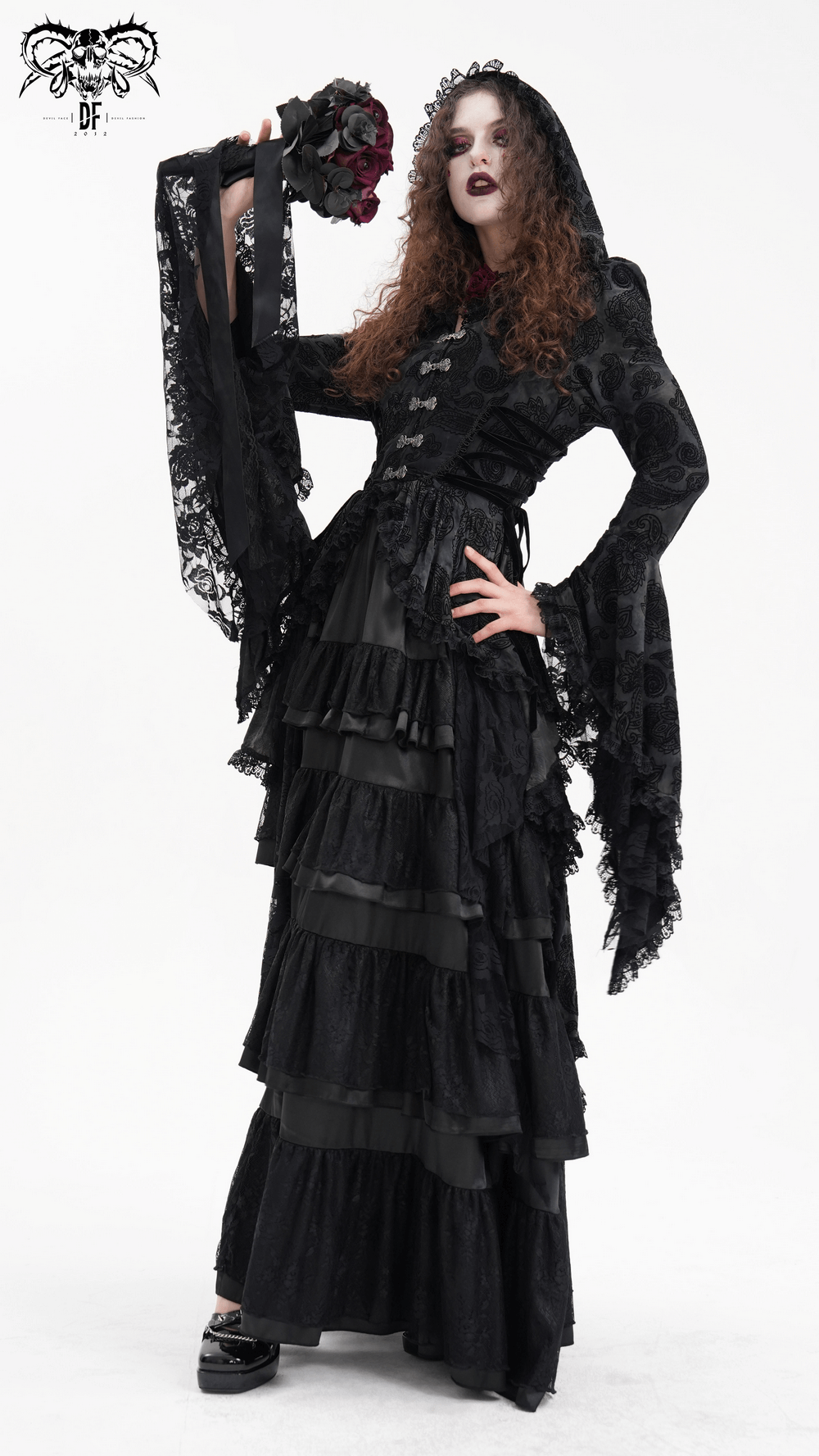 Elegant model in Gothic Victorian hooded lace cape with asymmetrical hem and layered black dress, holding a bouquet.