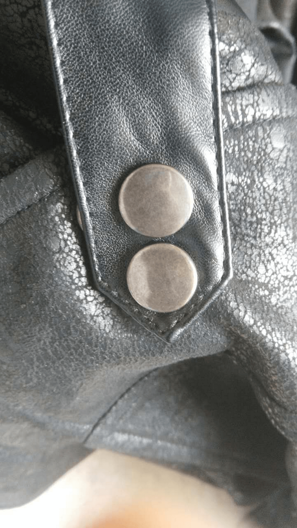 Close-up of black PU leather coat with silver snap buttons highlighting gothic vintage style.