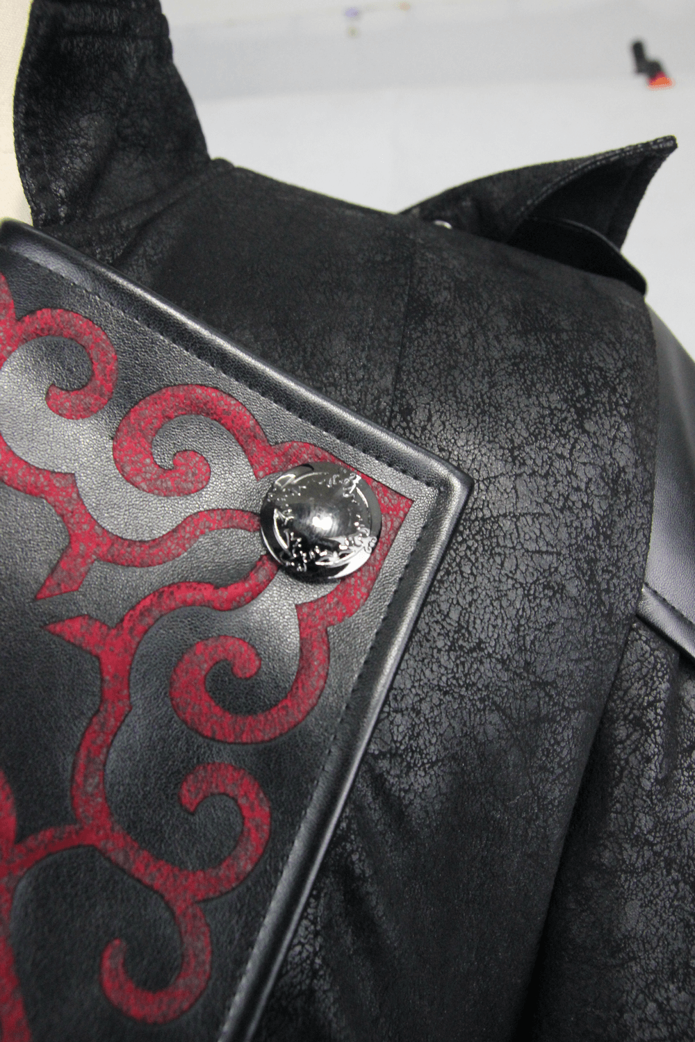 Close-up of Gothic vintage black coat with intricate red designs and stylish button details.