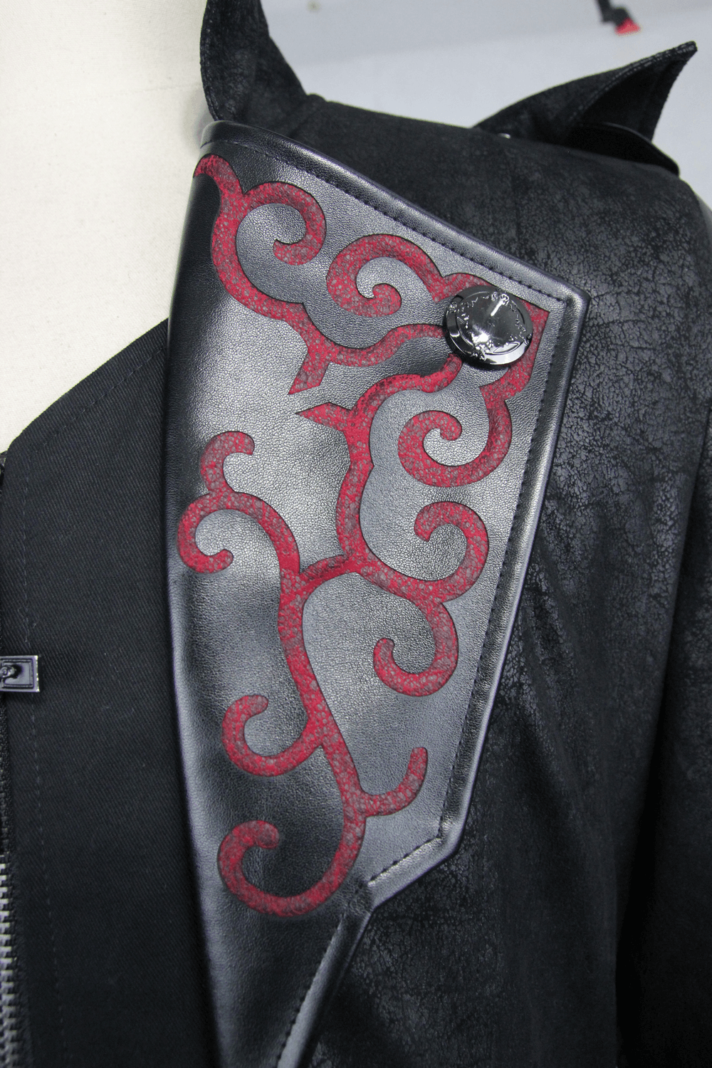 Close-up of gothic vintage long black coat detailing with ornate red designs and stylish button.