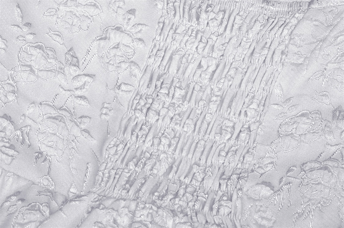 Close-up of white fabric featuring intricate floral embroidery and smocked detailing.
