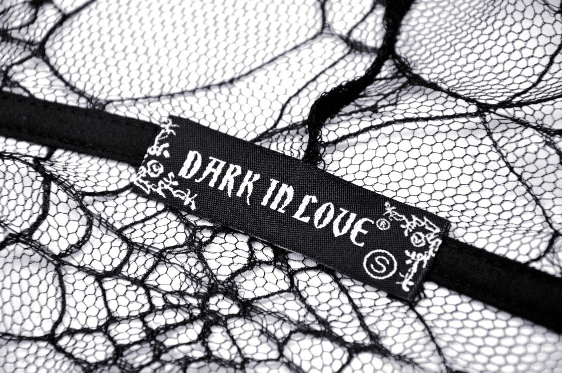 Close-up of 'Dark In Love' tag on sheer black lace fabric, perfect for gothic fashion enthusiasts.