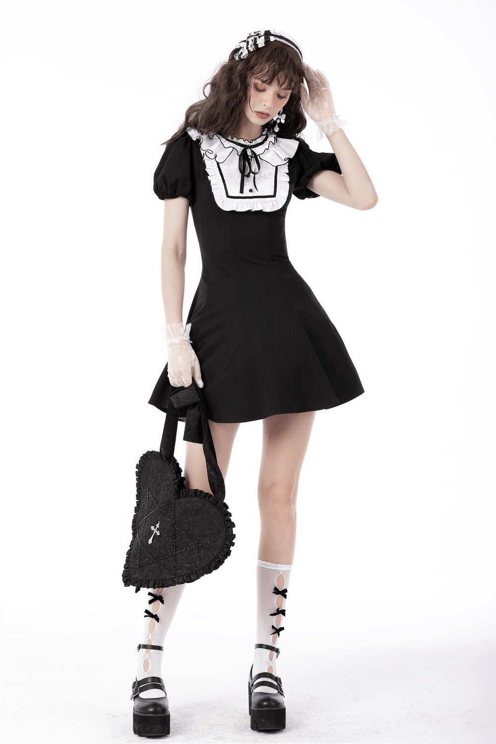 Gothic woman in black dress holding heart-shaped shoulder bag with cross detail, showcasing punk rock style.