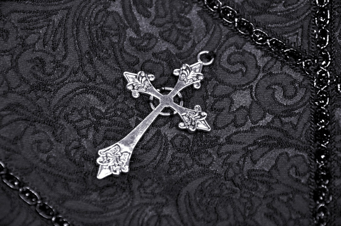Close-up of a delicate silver cross detail on a black patterned fabric, perfect for gothic fashion lovers.