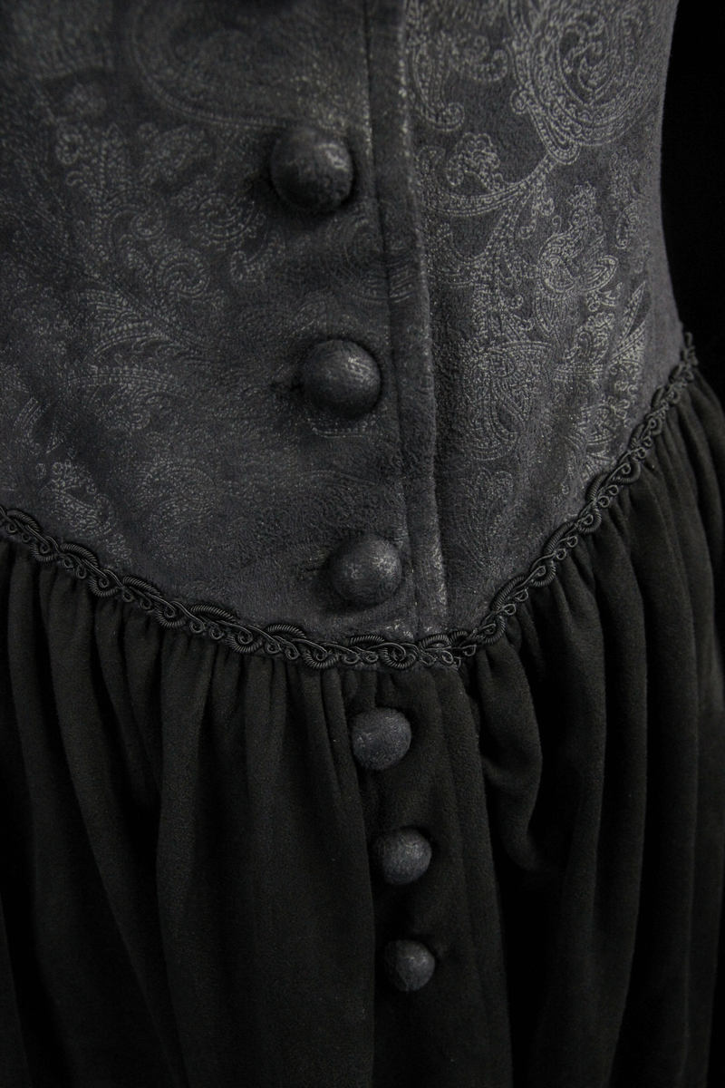 Close-up of gothic women's coat fabric with ornate patterns and large buttons, showcasing elegant design details.
