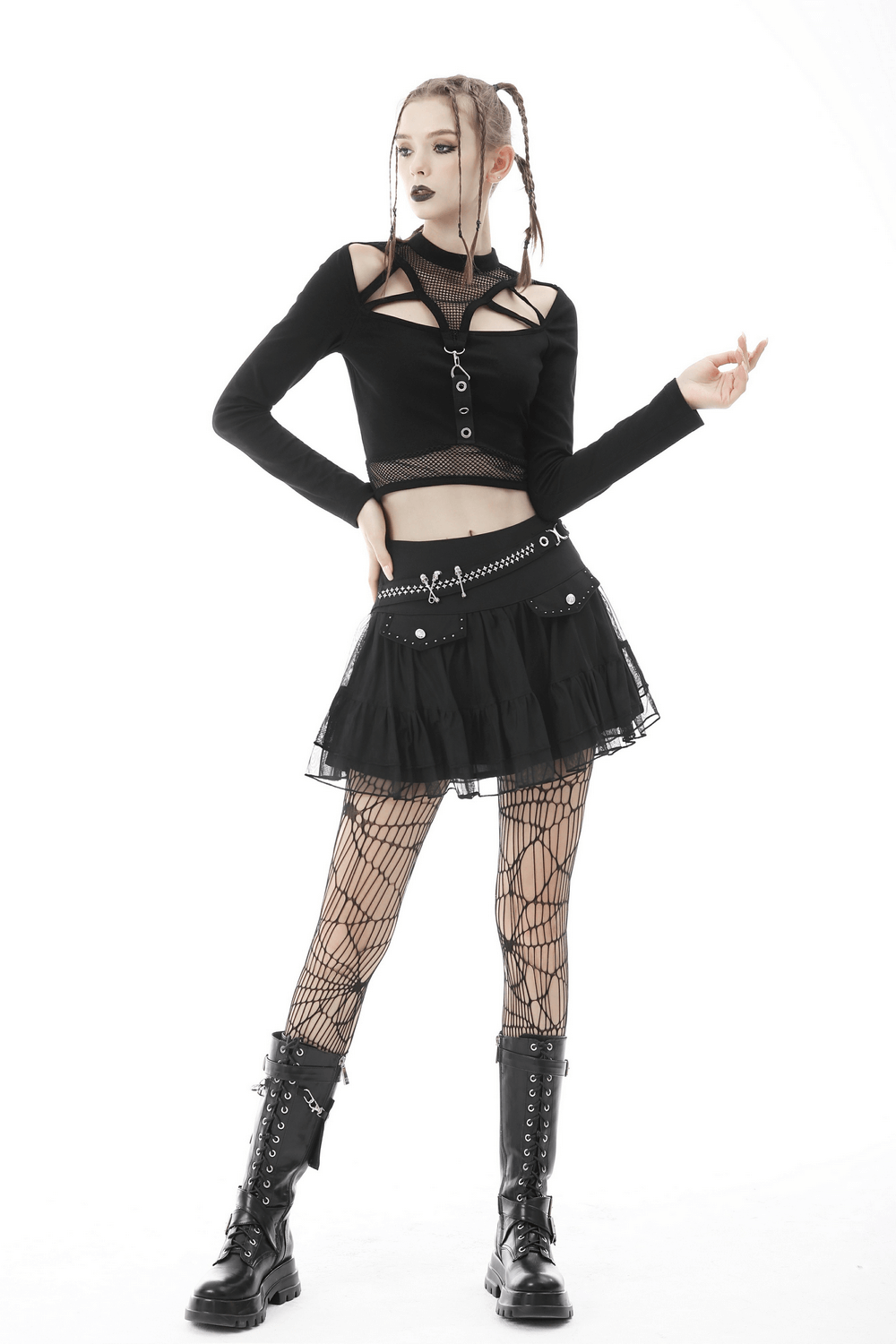 Gothic woman in a black cropped top and short pleated skirt showcasing chains, studs, and fishnet stockings.