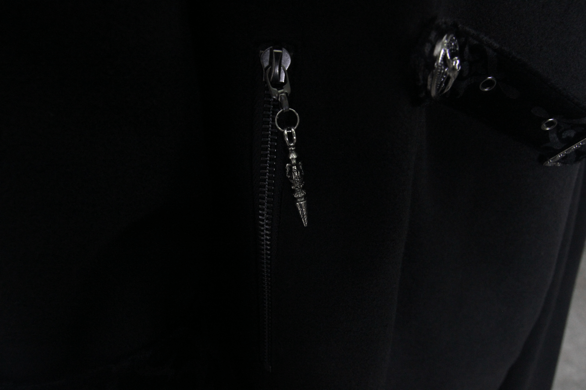 Close-up of gothic zipper detail on black trench coat for men, featuring a unique skull pull tab.