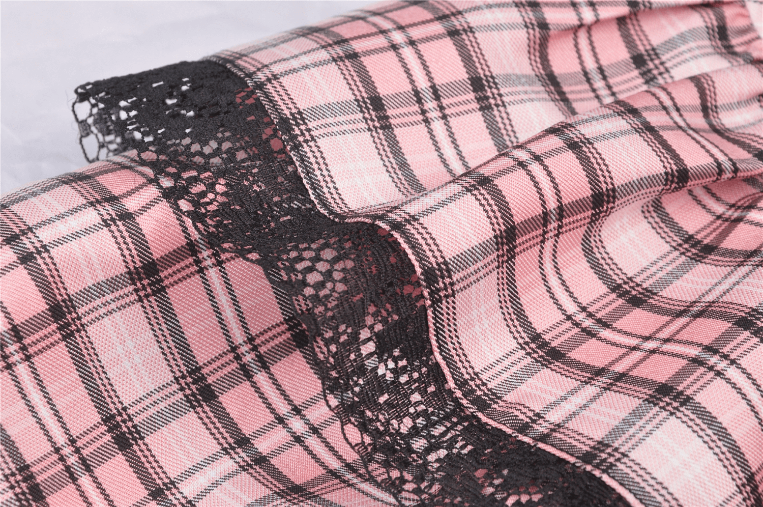 Close-up of pink and black plaid fabric with lace trim for a stylish grunge female mini skirt.