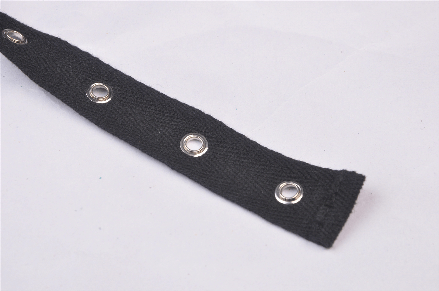 Close-up of a black fabric strap with metal grommets, perfect for punk rock fashion accessories and edgy outfits.