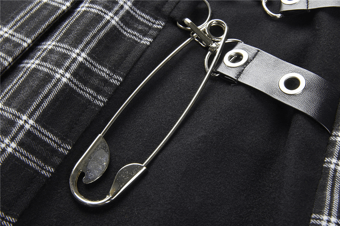 Close-up of a large silver safety pin accent on a black and white plaid skirt with grommet details.