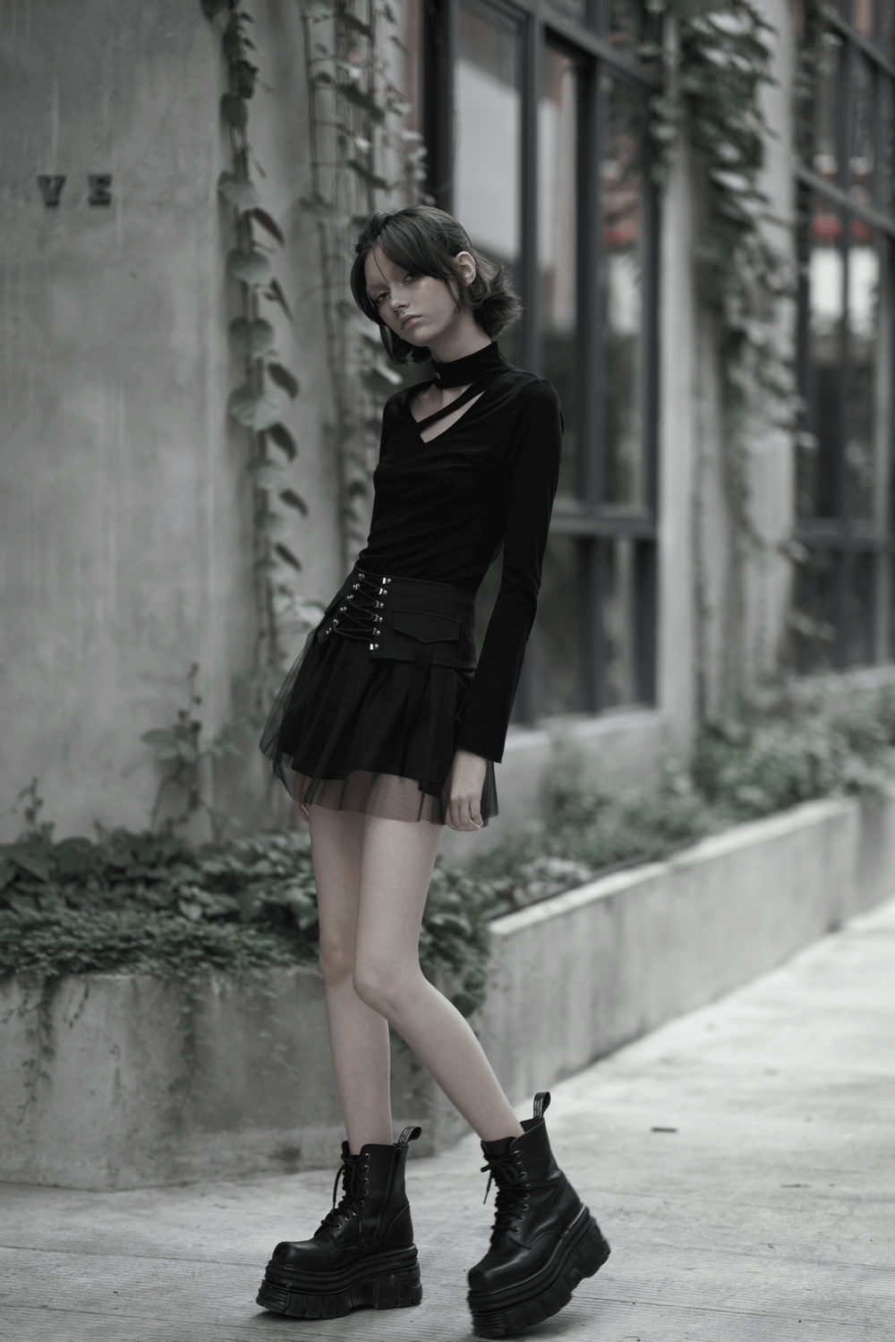 Model in a black long-sleeve top and high-waist black gothic skirt, featuring lace-up details and chunky boots.