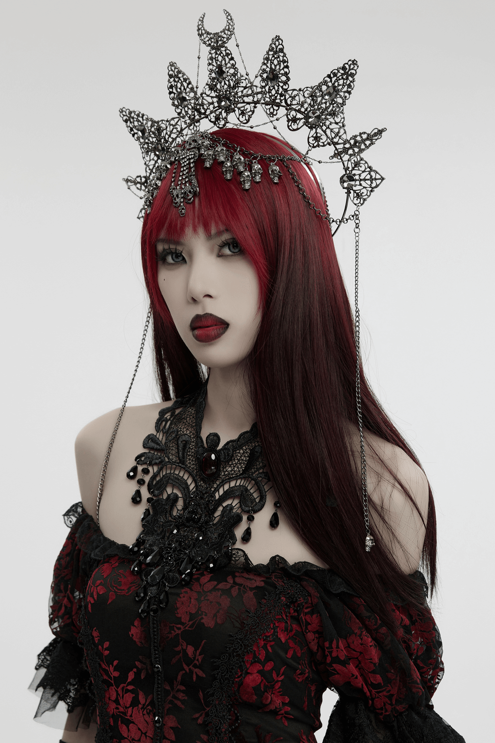 Gothic metal crown with skull pendants and chains, adorned with gemstones, worn by a model with red hair.