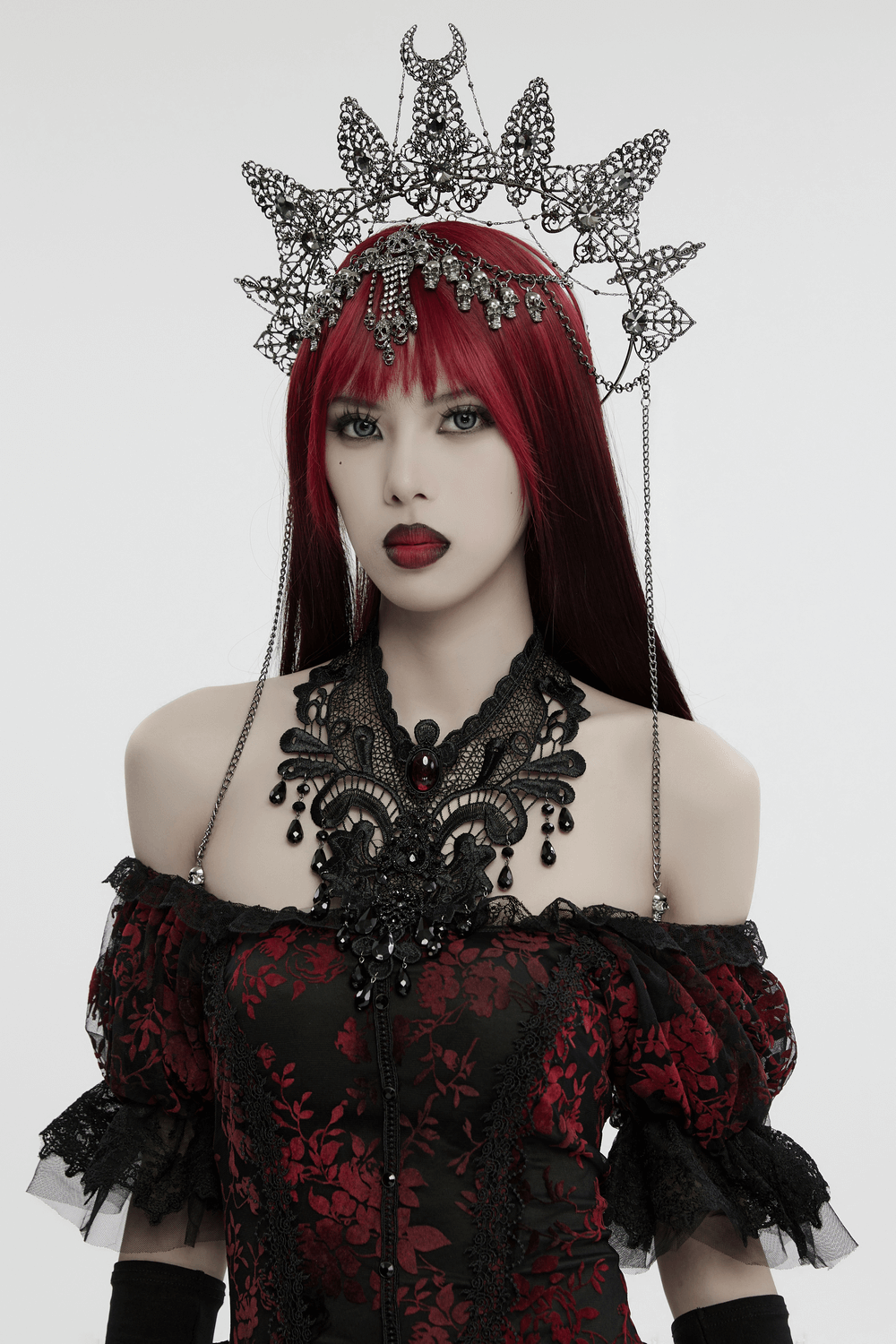 Gothic crown with skull pendants and chains, adorned with gemstones, worn by a model in a dramatic outfit.