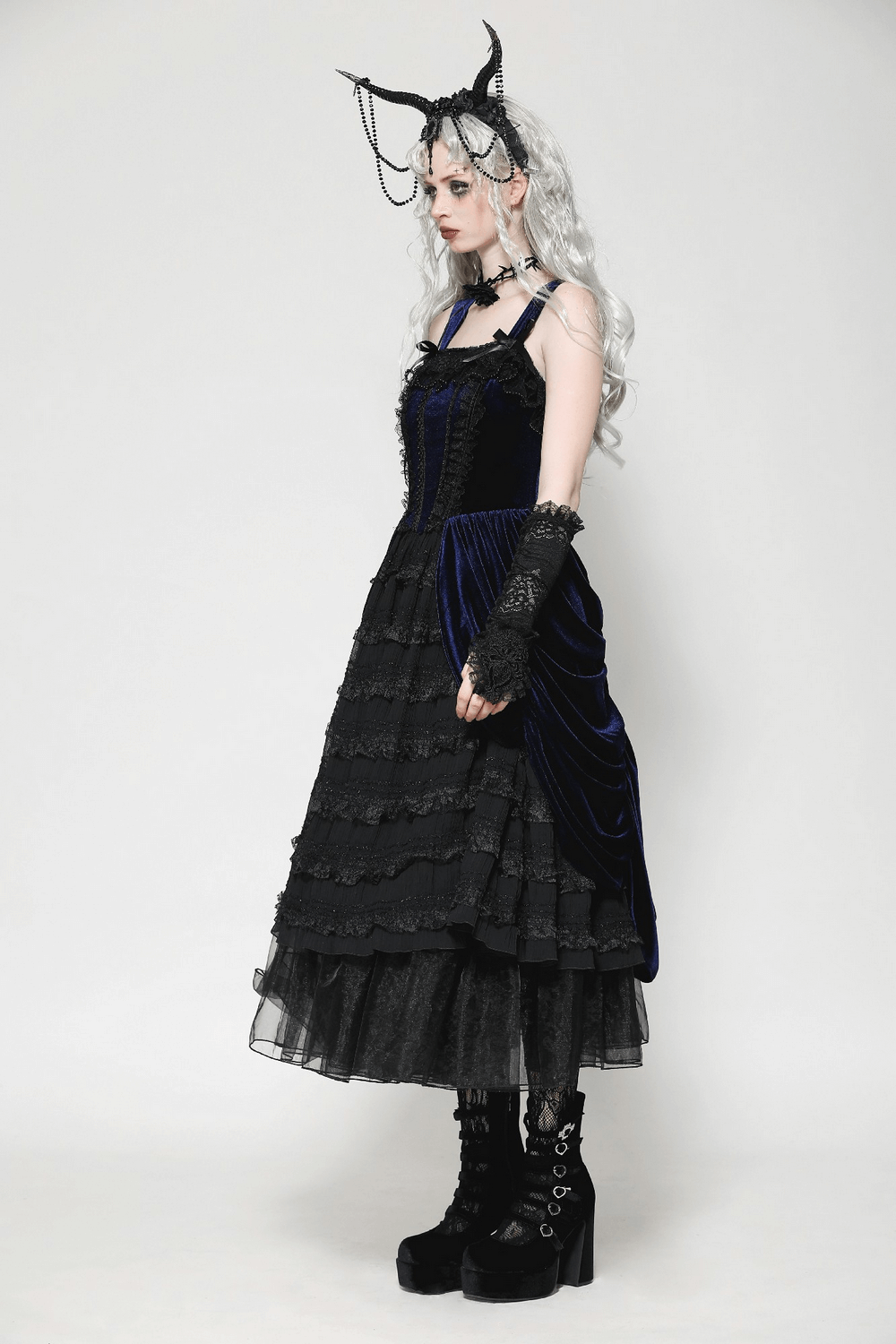 Gothic fashion model in a black and blue layered dress with lace gloves and dramatic high-heeled boots.